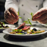 Chef adding the final flourish by adding some liquorice flavoured  parsley to the dish. The dish is, pan fried pink duck breast onto a bed of parsnip puree with seasonal autumn vegetables and berries. Colour, horizontal with some copy space, photographed on location in a restaurant on the island of Møn in Denmark.